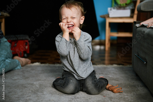 A little boy plays with his animal toys on a gray carpet. Child at home