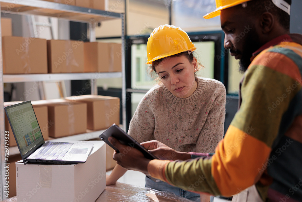 Diverse coworkers checking online orders on tablet computer, analyzing products for inventory report in warehouse. Stockroom team working at customers packages preparing transportation Diverse coworkers checking online orders on tablet computer, analyzing products for inventory report in warehouse. Stockroom team working at customers packages preparing transportation