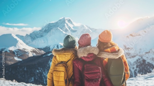 Four happy friends are standing and embracing against snow capped mountains at sunny day. Winter vacations concept photo