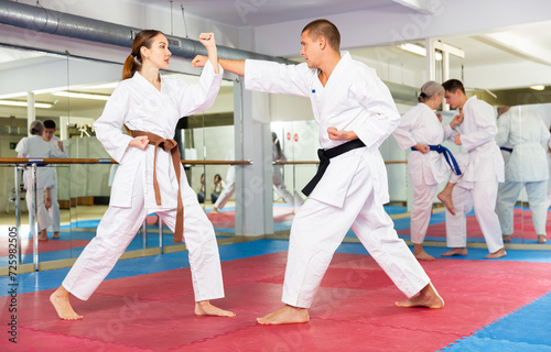 Caucasian man and woman in kimono sparring during group karate training. Senior woman and teenage boy fighting in background.