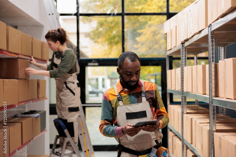 Warehouse employee analyzing merchandise checklist before start preparing clients packages for delivery. Storage room supervisor working with cardboard boxes during products quality control