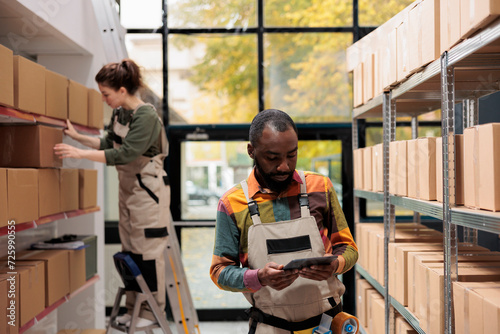 Warehouse employee analyzing merchandise checklist before start preparing clients packages for delivery. Storage room supervisor working with cardboard boxes during products quality control