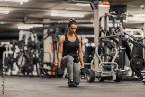 A sportswoman is lifting weights and doing lunges in a gym.