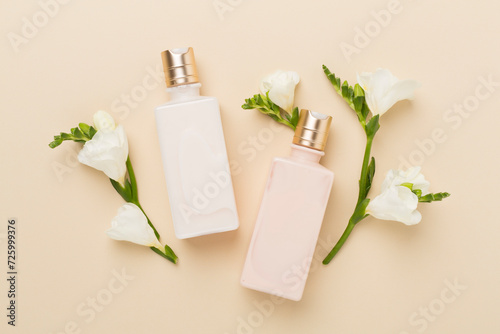 Cosmetic bottle with freesia flowers on color background, top view