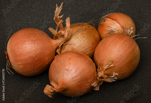 Onions unpeeled od dark grey background, horizontal.