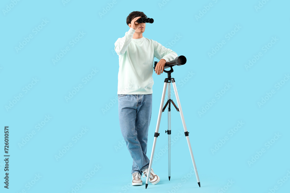 Young man with telescope and binoculars on blue background