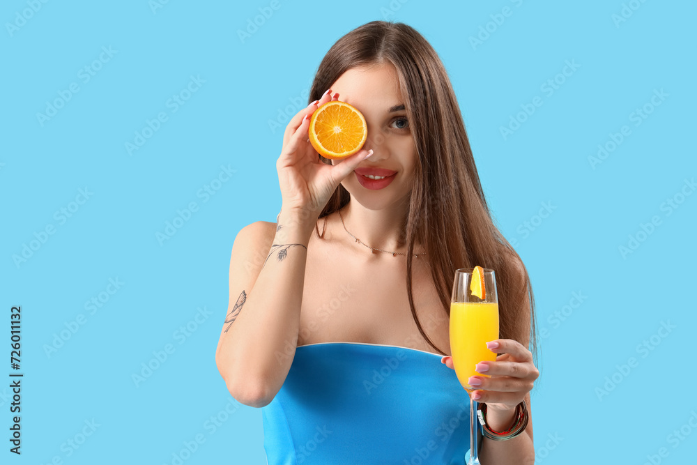 Beautiful young woman with glass of tasty citrus cocktail and orange piece on blue background Beautiful young woman with glass of tasty citrus cocktail and orange piece on blue background