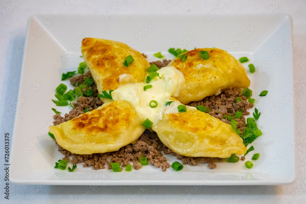 Traditional Ukrainian pierogi grilled in butter and served with minced meat and cream, decorated with fresh fine herbs Traditional Ukrainian pierogi grilled in butter and served with minced meat and cream, decorated with fresh fine herbs
