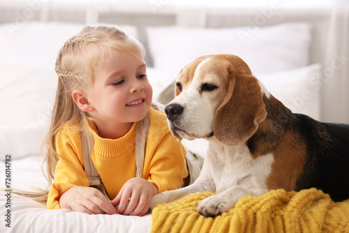 Cute little girl with Beagle dog in bedroom, closeup