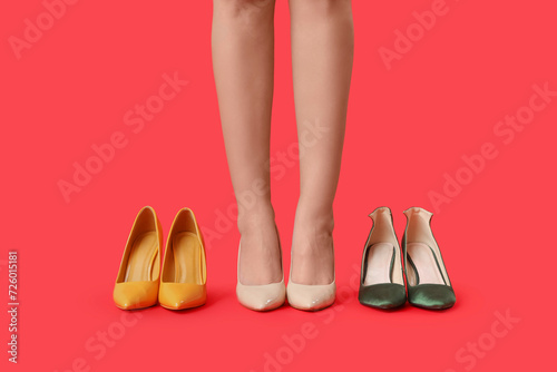 Legs of young woman in stylish beige high heels and different shoes on red background
