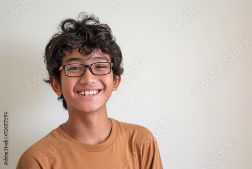 A young boy wearing glasses and a brown shirt smiles for the camera photo