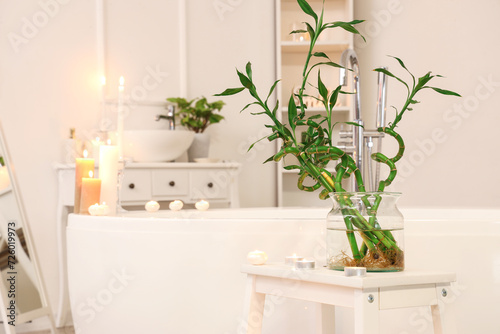 Vase with bamboo stems and burning candles on stool in bathroom