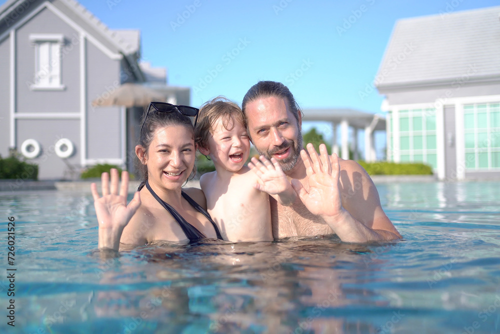 Happy Caucasian White people family, father, mother and son, are enjoy playing water in the swimming pool.