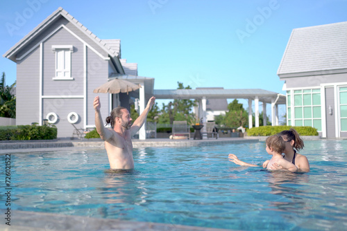 Happy Caucasian White people family, father, mother and son, are enjoy playing water in the swimming pool. © DG PhotoStock