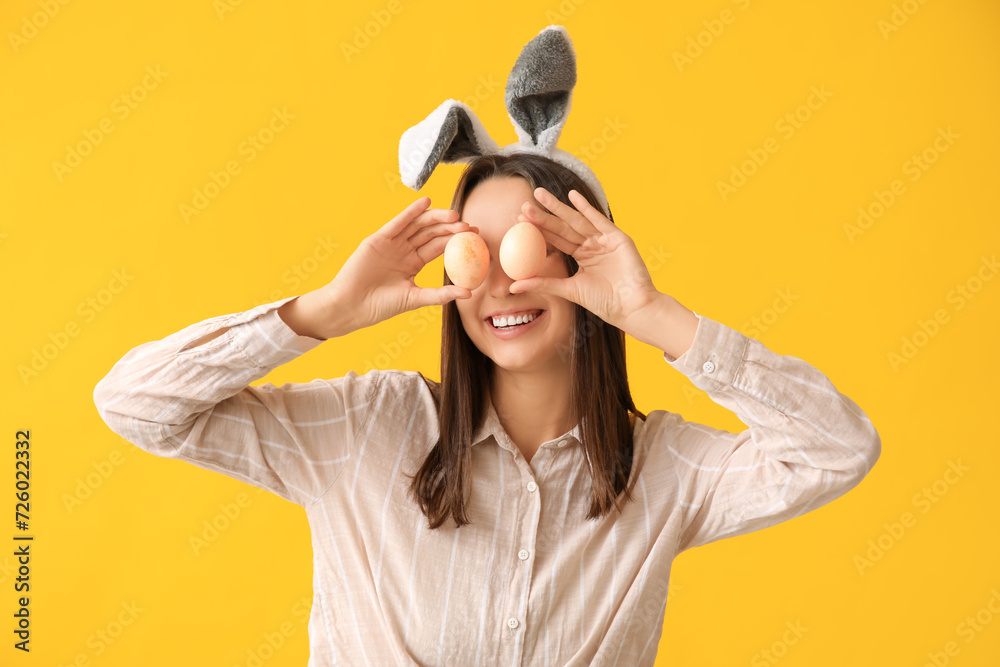 Funny young woman with bunny ears and Easter eggs on yellow background Funny young woman with bunny ears and Easter eggs on yellow background