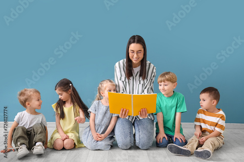 Little children with nursery teacher reading book near blue wall