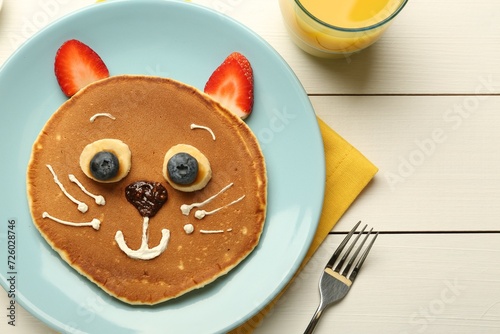 Creative serving for kids. Plate with cute cat made of pancakes, berries, cream, banana and chocolate paste on white wooden table, top view. Space for text