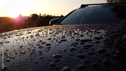 Hood of car with big water droplets after warm heavy summer rain. Sunset backlight shine in every drop. Close up slow panning video