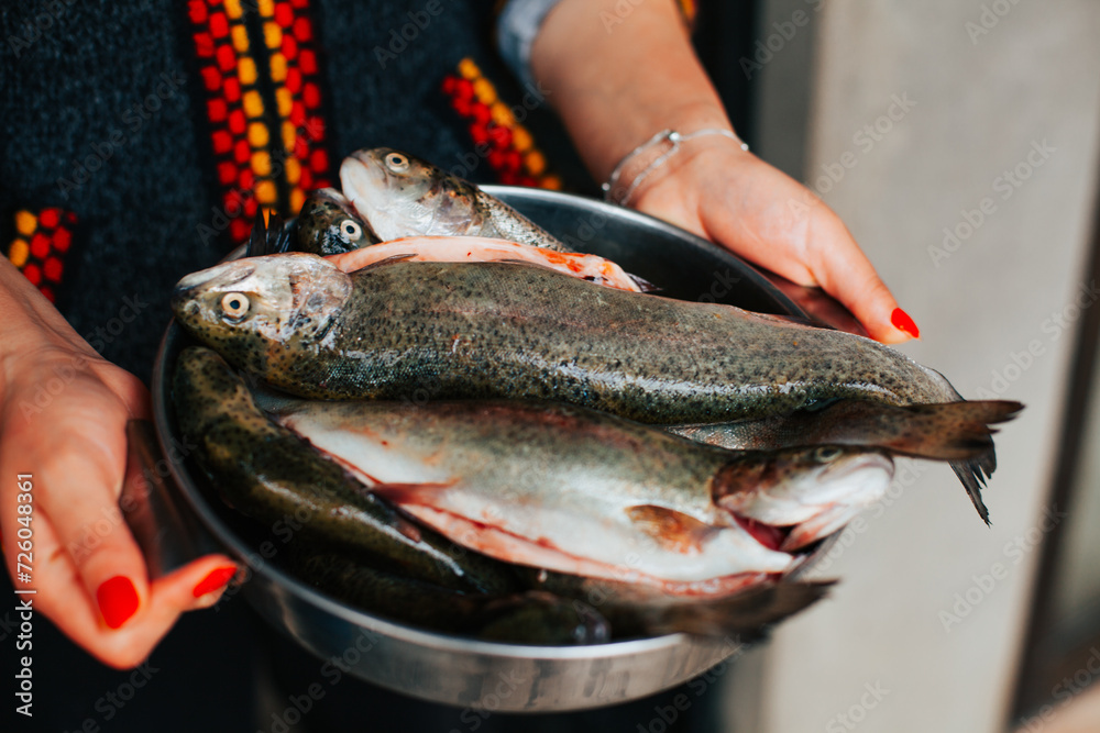 Photograph of anonymous hands with many trout in a bowl. Concept of food preparation.