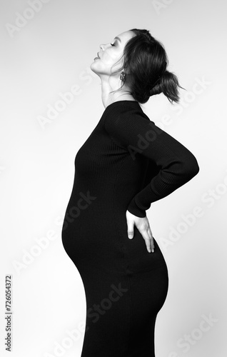 Black and white portrait of young pregnant female in black dress.