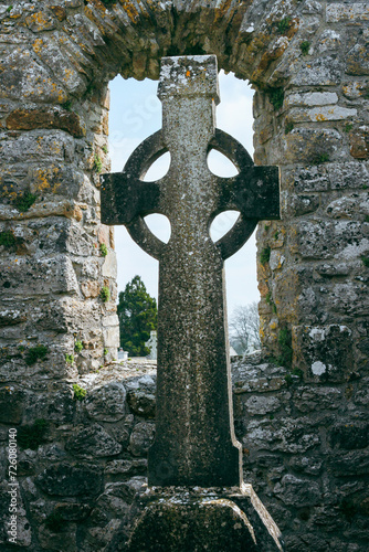 Celtic cross framed by ancient stone ruin walls with blue sky, Clonmacnoise, Ireland