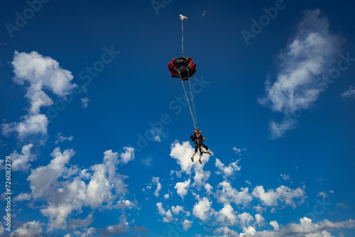 Tandem skydive pair deploy parachute in blue sky and clouds