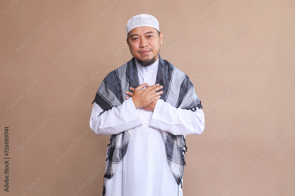 Grateful muslim man keeping both hands on chest, expressing gratitude and appreciation on beige background Grateful muslim man keeping both hands on chest, expressing gratitude and appreciation on beige background