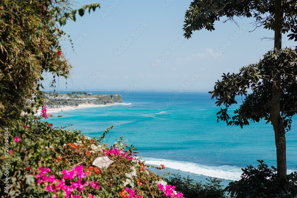 Beautiful view of the azure ocean and waves against the background of flowers and trees.