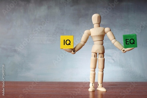 Wooden human figure balancing wooden cubes with text IQ and EQ. Copy space for text.