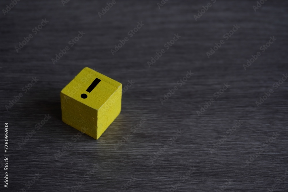 Yellow wooden cube on table with exclamation mark icon. Copy space for text. Yellow wooden cube on table with exclamation mark icon. Copy space for text.