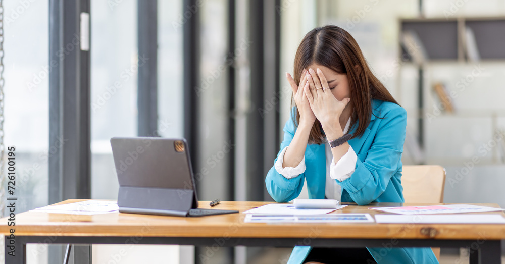 Obraz premium Shot of stressed, sleepy and bored business asian woman sitting at a desk on laptop for a long time and looking worried, tired and overwhelmed