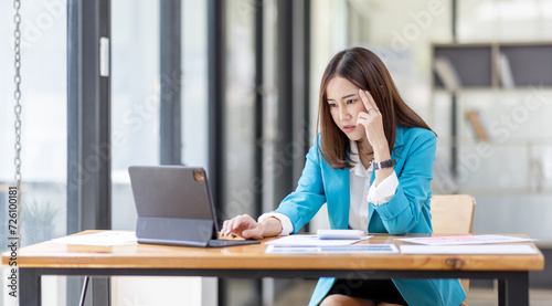 Shot of stressed, sleepy and bored business asian woman sitting at a desk on laptop for a long time and looking worried, tired and overwhelmed © David