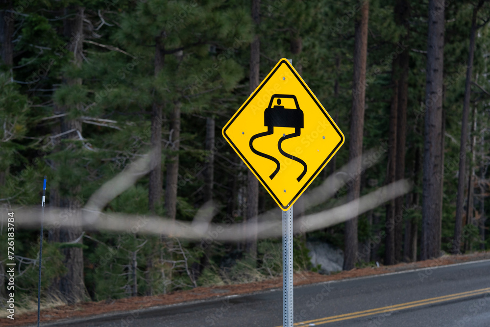 Slippery when wet road sign with forest backdrop. Vertical. Slippery when wet road sign with forest backdrop. Vertical.