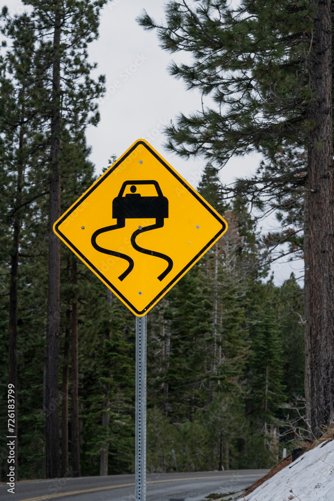 Slippery when wet road sign with forest backdrop. Vertical. Slippery when wet road sign with forest backdrop. Vertical.