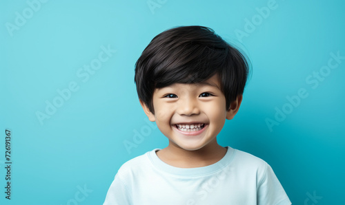 Joyful Asian child with bowl-cut black hair wearing a pale blue shirt on a matching studio background  smiling brightly