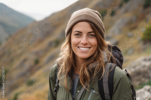 Portrait of a smiling young woman with backpack looking at camera in the mountains