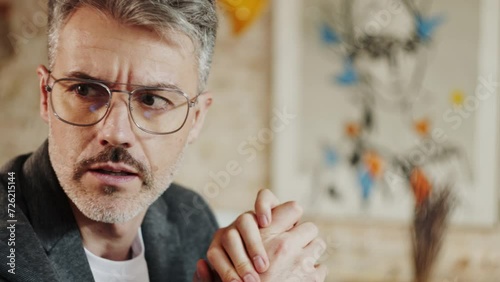 handsome businessman with bristle and moustache in eyewear talking to his business colleague with hands crossed. He is nodding and smiling. Blurred painted in the background. photo
