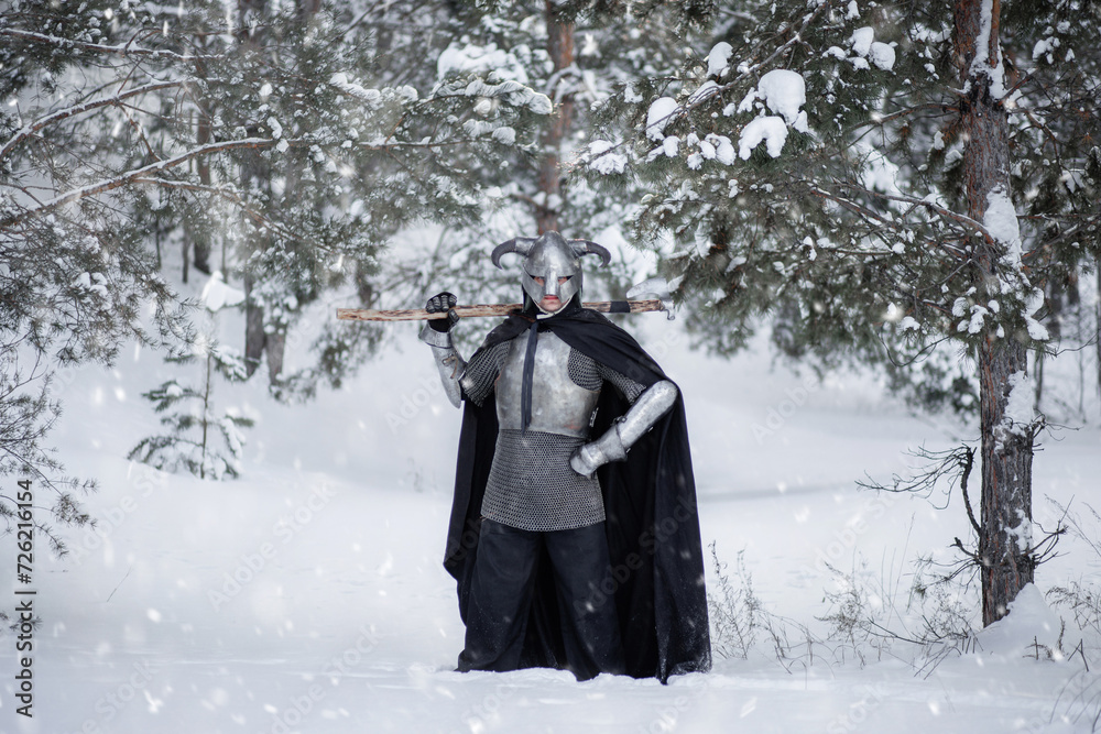 Full-length portrait of a medieval fantasy warrior in a horned helmet, steel breastplate, chain mail with a two-handed ax in his hands, posing against the backdrop of a winter forest.