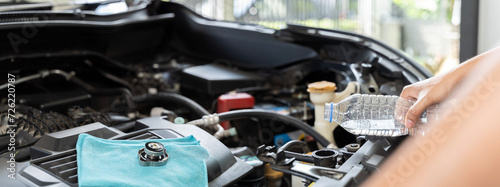 A person is pouring water into a car radiator. The person is trying to cool down the car engine.