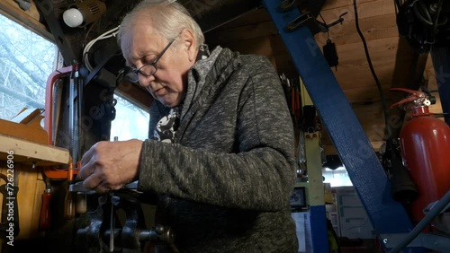 Senior mechanic uses Vernier caliper to measure machine part held in a bench vice photo