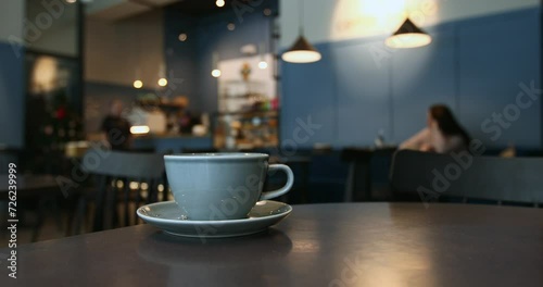 Close-up of a blue porcelain cup, atmosphere of a coffee shop in bokeh background, unrecognizable people moving, lifestyle horizontal video with copy space