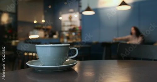 Close-up of a blue porcelain cup, atmosphere of a coffee shop in bokeh background, unrecognizable woman drinking water, lifestyle horizontal video with copy space