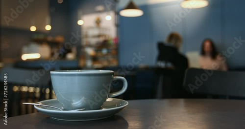 Close-up of a blue porcelain cup, atmosphere of a coffee shop in bokeh background, unrecognizable guests chatting, lifestyle horizontal video with copy space