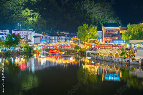 View of the lake in the ancient and touristy Chinese town of Yangshuo with reflections in the water and surrounded by the restaurants, cafes and shops of the well-known West Street (Xi Jie) at night.