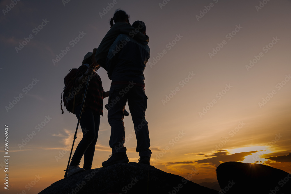 Silhouette of hiker family on the top of mountain on sunset
