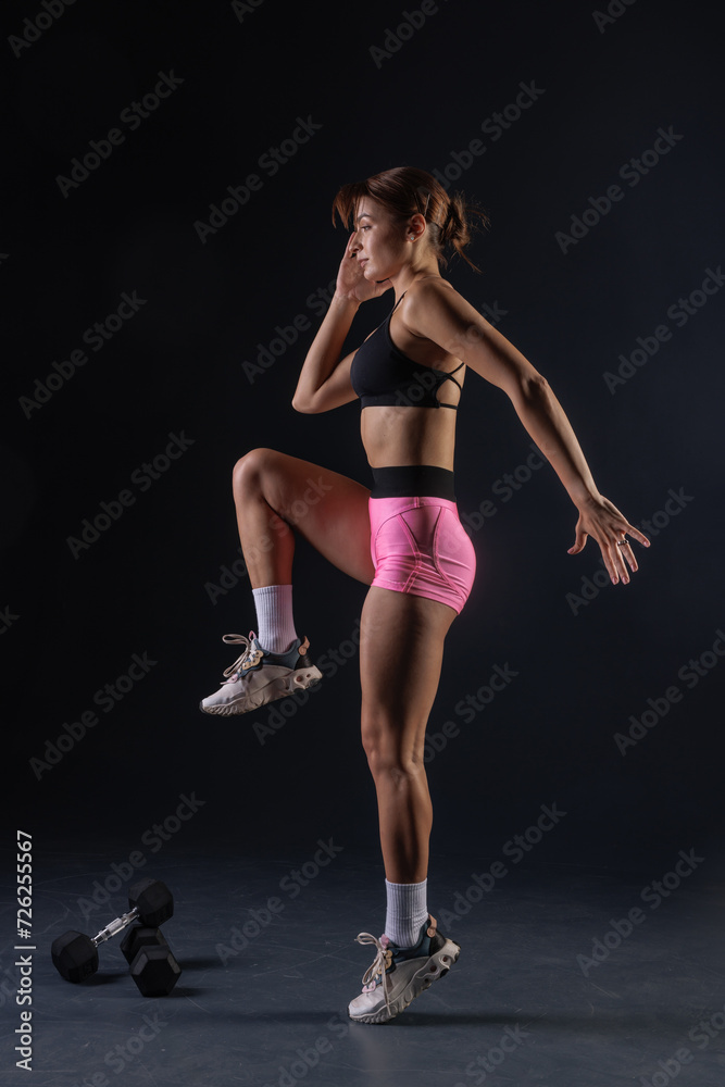 athletic girl doing exercise with dumbbells on black background, sports concept