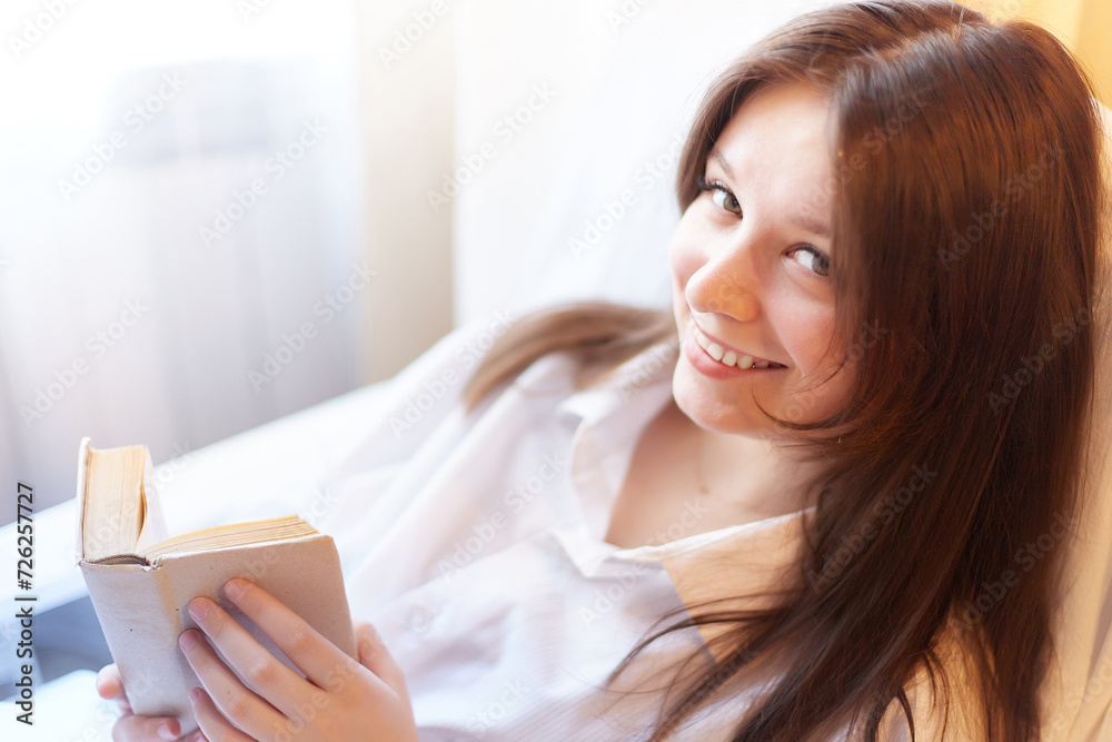 Cute brunette girl is reading small book of poetry in bedroom in morning. Young pregnant woman in the maternity hospital with a book of tips on parenting. A sick and recovering lady Cute brunette girl is reading small book of poetry in bedroom in morning. Young pregnant woman in the maternity hospital with a book of tips on parenting. A sick and recovering lady