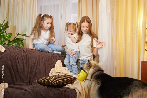 Loving family with mother, daughter sisters and big dog in living room. Woman mom, small child girl, female teenager who is afraid of a big pet
