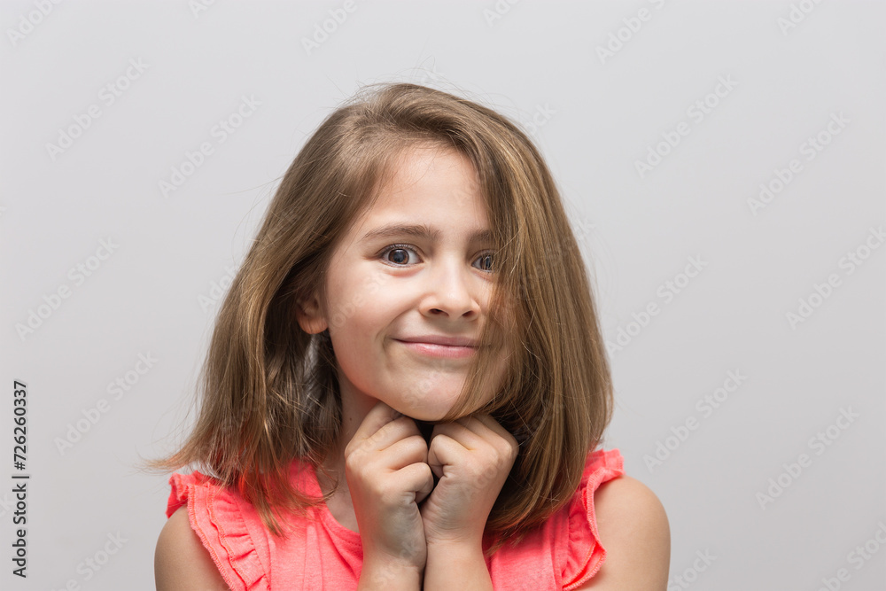 Little 8 years old with cheerful and smiling, with light brown hair and salmon color t-shirt with hands together under chin on white background. Concept of children and childhood