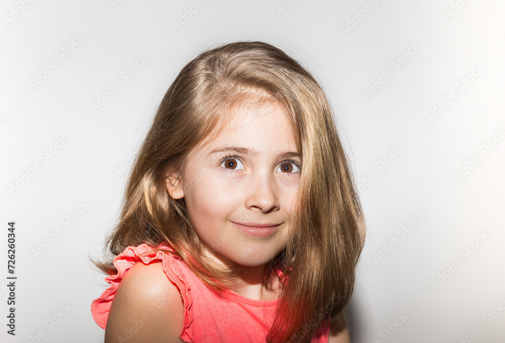 Close up portrait of 8 years old little girl smiling looking up with salmon color t-shirt and light hair loose and white background. Children and childhood concept Close up portrait of 8 years old little girl smiling looking up with salmon color t-shirt and light hair loose and white background. Children and childhood concept